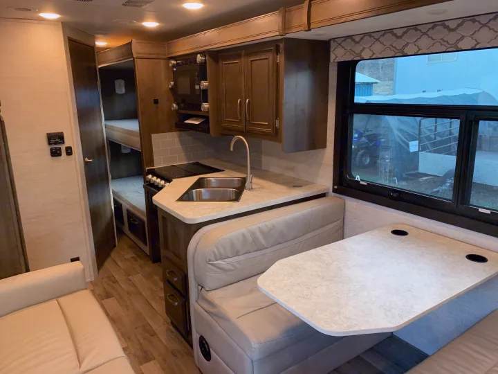 Spacious RV rental interior with a modern kitchen, dinette, and bunk beds, offering a comfortable living space.. Jayco Redhawk 2021