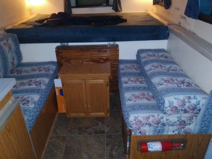 RV rental interior featuring a bed, floral dinette seating, and a wooden cabinet. Fire extinguisher visible for safety.. K-Z Manufacturing Coyote 2002