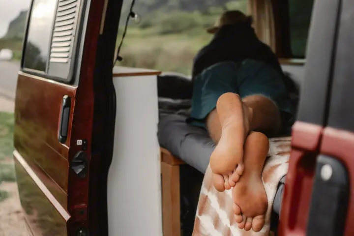 A person's bare feet are seen relaxing inside an RV rental, looking out at a scenic road and landscape. Perfect van life.. Volkswagen Eurovan 2003
