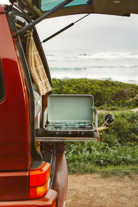 Enjoy outdoor cooking with this rv rental! A camper van's pull-out stove with ocean waves in the background.. Volkswagen Eurovan 2003