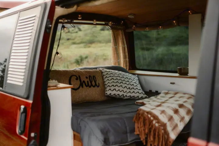 Comfortable RV rental interior with a bed, 'Chill' pillow, string lights & a window view of nature. Perfect for van life.. Volkswagen Eurovan 2003