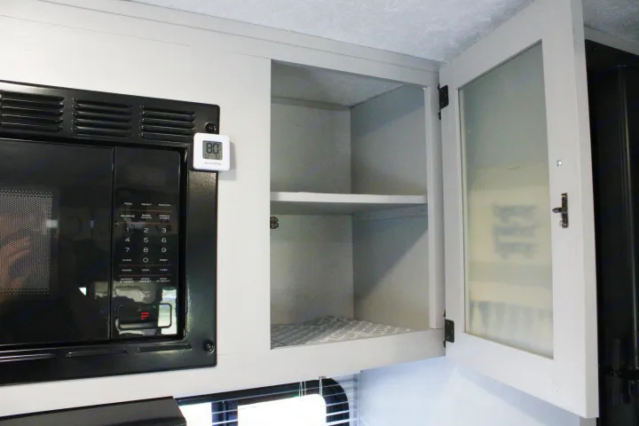 Inside an rv rental kitchen: a black microwave, open gray cabinets, and a digital thermometer showing 80°F.. Forest River Salem FSX 2021