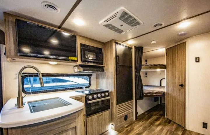 Modern RV rental interior with a kitchen (sink, stove, microwave, fridge) and bunk beds. Ideal for travel and camping.. Keystone RV Passport SL 2021