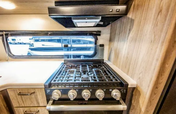 RV rental kitchen: a functional space with gas stove/oven, range hood, and window view.. Keystone RV Passport SL 2021