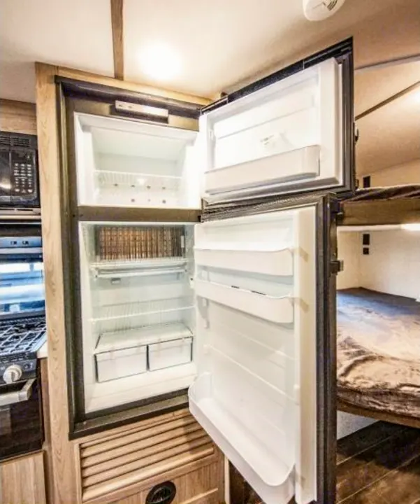 RV rental's functional interior: open two-door fridge, kitchen stove, and cozy bunk beds.. Keystone RV Passport SL 2021