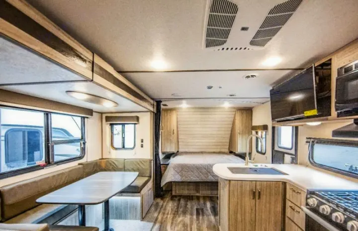 Interior of a modern RV rental, featuring a compact kitchen, dinette, bedroom, and ceiling AC unit.. Keystone RV Passport SL 2021