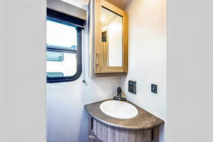 This clean RV rental bathroom features a corner sink, mirrored cabinet, and window, offering practical amenities.. Keystone RV Passport SL 2021