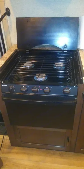 This black Dometic stove and oven unit, a key RV rental kitchen appliance, features three stovetop burners and control knobs.. Thor Freedom Elite 2018