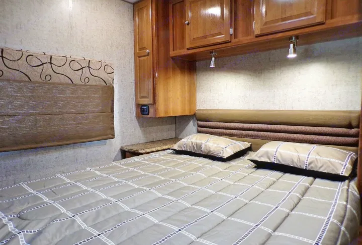 Cozy RV rental bedroom interior with a comfortable bed, patterned comforter, overhead cabinets, and reading lights.. Coachmen Leprechaun 2018