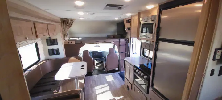 Bright rv rental interior, showing kitchen with fridge, stove, and microwave, a dining booth, and an over-cab sleeping area.. Forest River Sunseeker 2020