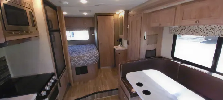 Inside an RV rental: full kitchen, comfy bed, and dining booth with ample storage for your road adventures.. Forest River Sunseeker 2020