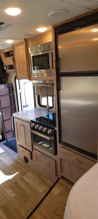 View of a clean, modern RV rental kitchen featuring a stainless steel refrigerator, microwave, range, and sink.. Forest River Sunseeker 2020