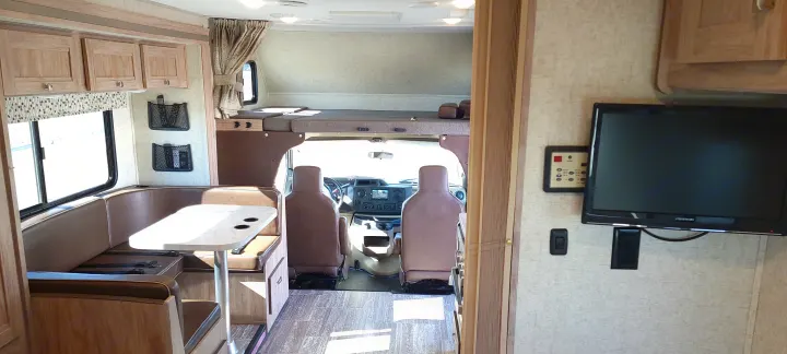 Inside an RV rental, a spacious interior view from the side showing the dinette, overhead bunk, and cockpit.. Forest River Sunseeker 2020