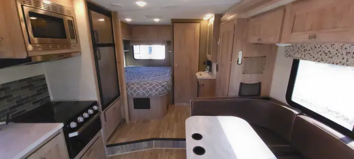 This bright rv rental interior showcases a full kitchen with microwave & stove, a bedroom with a bed, and a comfortable dinette.. Forest River Sunseeker 2020