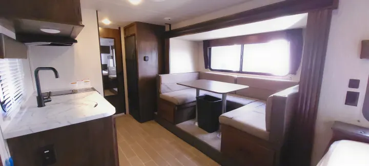 This RV rental interior features a functional kitchen with a sink, alongside a cozy U-shaped dinette with bright windows.. Forest River Wolf Pup 2020