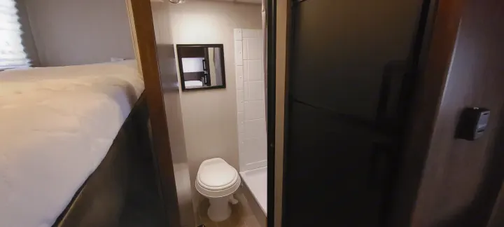 Compact RV rental interior featuring a comfortable bed, a small bathroom with a toilet and shower, and a refrigerator.. Forest River Wolf Pup 2020