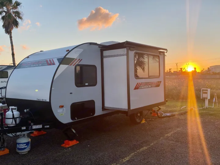 RV rental: Gray & white Platinum Wildwood FSX travel trailer parked at a campsite, bathed in warm sunset light.. Forest River Wildwood 2021
