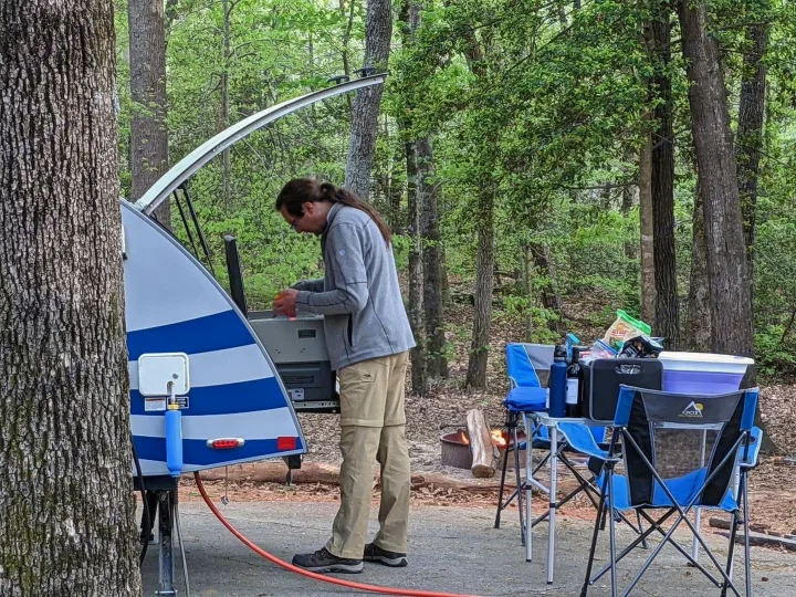 Prepping a meal in an RV rental! A person uses a teardrop camper's rear kitchen at a serene, wooded campsite.. T@G T@G Trailer 2016