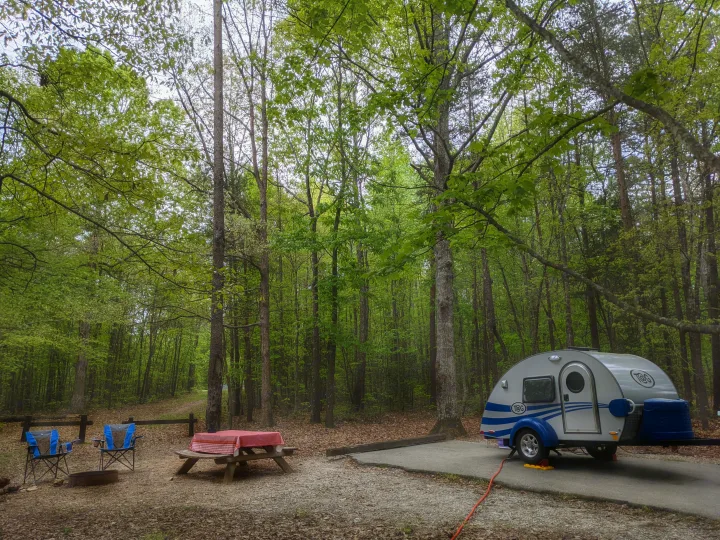 Serene campsite with a teardrop RV rental parked on a paved pad, complete with a picnic table and lush trees.. T@G T@G Trailer 2016