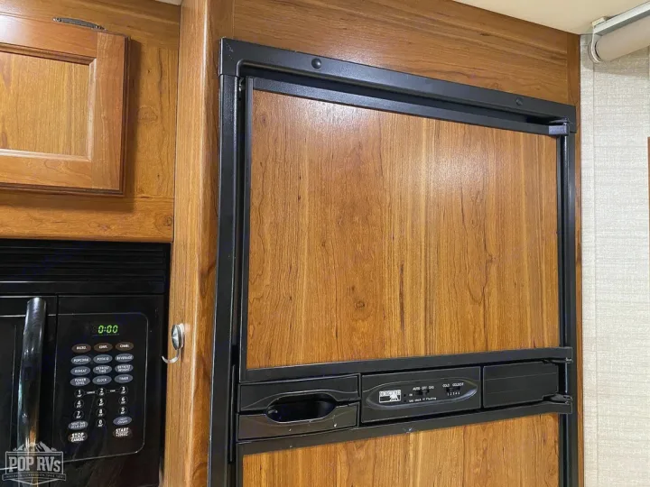 Inside an RV rental: a sleek wood-paneled refrigerator and a compact microwave integrated into warm wooden cabinetry.. Jayco Melbourne 2016