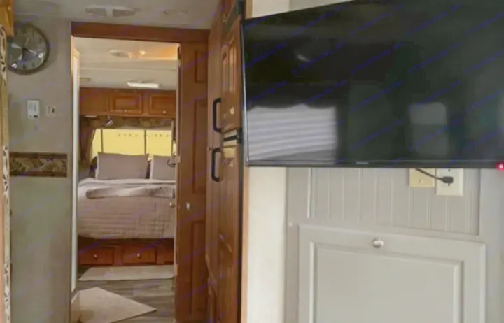 Inside an RV rental: a comfortable bedroom is visible through a doorway, with a TV and beadboard wall in the foreground.. Forest River Rockwood Ultra Lite 2009