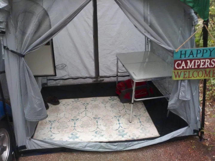 Inside an RV rental's cozy awning: a patterned rug, folding table, and a 'Happy Campers Welcome' sign greet visitors.. T@G T@G Trailer 2016