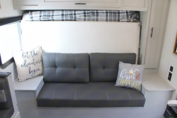 This RV rental's cozy interior features a gray sofa, clever wall-mounted bed, and adventure-themed pillows.. Forest River Salem FSX 2021