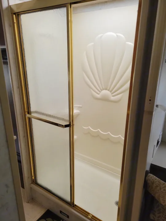 RV rental shower: See this compact shower with frosted glass doors, gold trim, and a unique seashell wall design.. Itasca Sundancer 2004