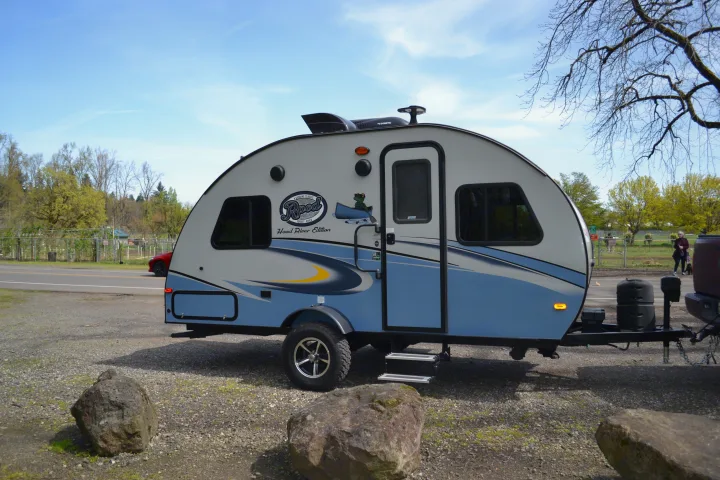 A light-colored R-Pod travel trailer, ideal for an rv rental, on a gravel lot with a scenic background.. R-Pod R177 2018