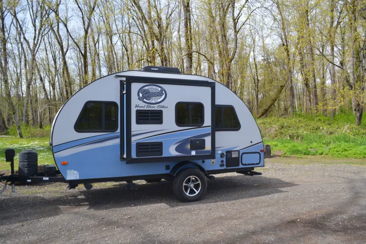 Light blue R-pod travel trailer, perfect for an rv rental, parked in a scenic forest setting on a gravel lot.. R-Pod R177 2018