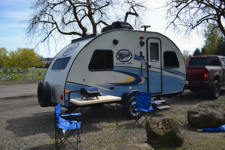 RV rental setup: R-Pod travel trailer, red truck, grill, & chairs arranged for outdoor leisure and camping.. R-Pod R177 2018
