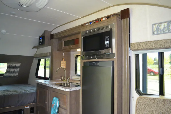 This rv rental interior features a full kitchenette with a microwave, sink, and fridge, plus a nearby sleeping area.. R-Pod R177 2018
