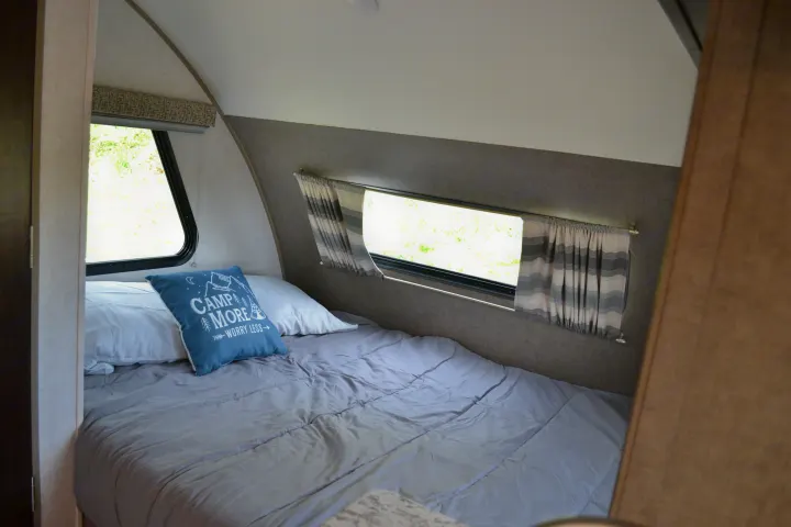 Comfortable sleeping area inside an RV rental, with a tidy grey bed, decorative pillow, and sunlit windows.. R-Pod R177 2018