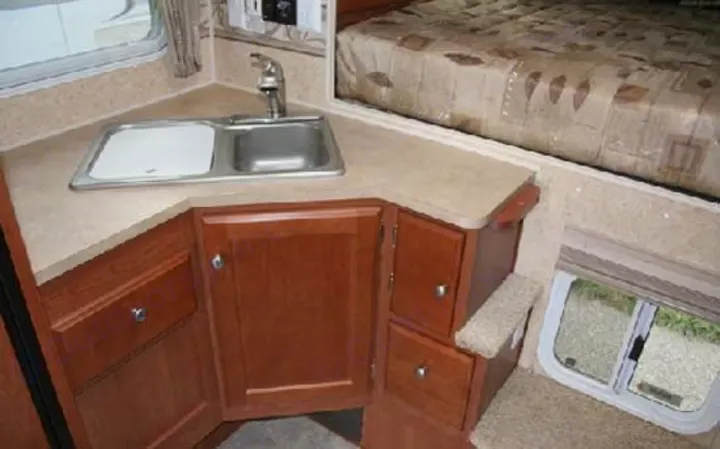 RV rental interior: Compact kitchen with sink, wood cabinets, and an elevated bed area with a side window.. Adventurer F350 2006