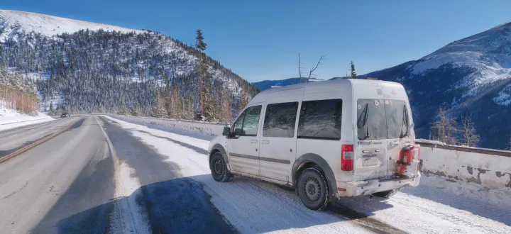 Winter mountain RV rental adventure: A white Ford Transit Connect van parked on a snowy road with pine forests.. Ford Transit Custom 2011