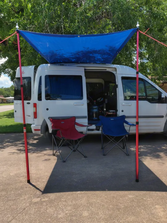 An RV rental camper van with a blue awning and chairs, creating a cozy outdoor camp setup.. Ford Transit Custom 2011