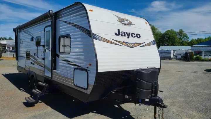 Clean Jayco travel trailer for rv rental. White & black RV with awning & steps, parked outdoors under a sunny sky.. Jayco Rocky Mountain 242BHSW 2019