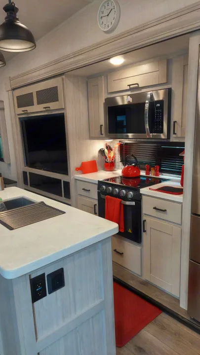 Modern RV rental kitchen showcasing light cabinetry, microwave, stove, island sink, and TV. Ideal for road trips.. East to West Tandara 2021