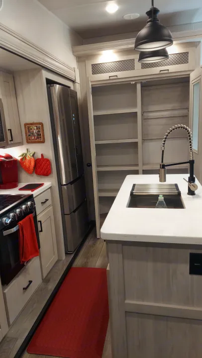 Bright, modern RV rental kitchen: sleek sink with spring faucet, gas stove, stainless fridge, and red accents on light cabinetry.. East to West Tandara 2021