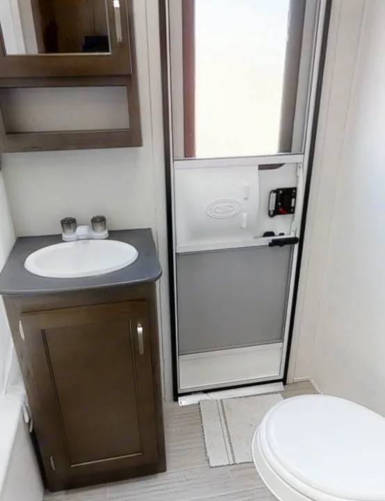 Compact RV rental bathroom showcasing a sink, vanity, overhead cabinet, toilet, and the main RV entry door.. Keystone Passport 2020