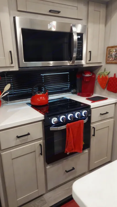 Step into this sleek RV rental kitchen, equipped with a microwave, modern stove, and vibrant red kettle for your travel meals.. East to West Tandara 2021