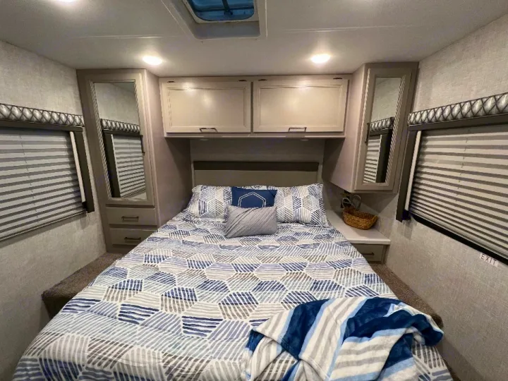 Cozy RV rental bedroom with geometric bedding, ample storage, and window blinds for comfortable travel.. Thor Quantum 2022