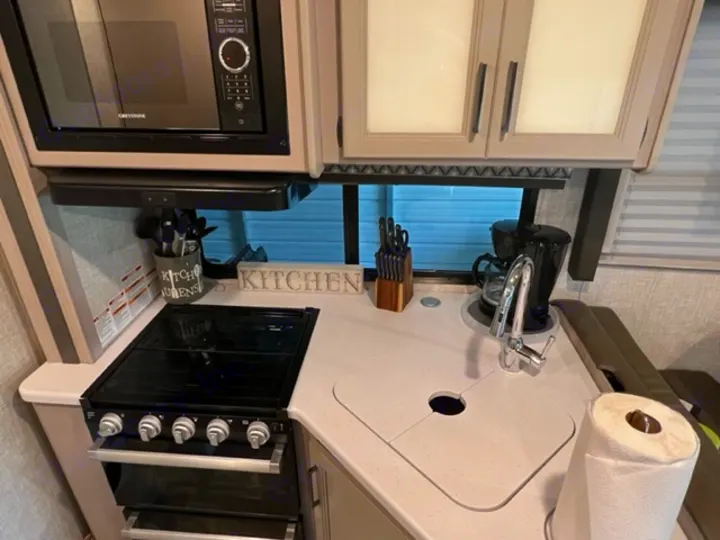 This RV rental kitchen features a microwave, stove, sink, and coffee maker, showing compact and functional amenities.. Thor Quantum 2022