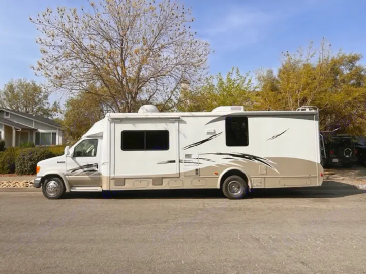 White and tan Class C RV rental motorhome parked on street, ready for travel.. Itasca Cambria 2008