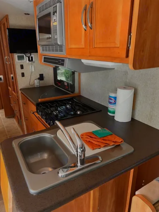 RV rental kitchen: Clean, functional space with microwave, gas stove, sink, and wood cabinets. Essential for travel cooking.. Itasca Cambria 2008