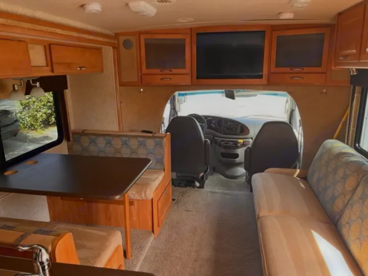 Interior view of an RV rental showing a dinette, sofa, overhead cabinets, and driver's cockpit.. Itasca Cambria 2008
