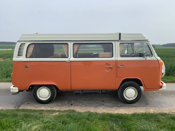 Vintage orange & white VW pop-top camper van for your next RV rental. Parked roadside near green fields.. Volkswagen westfalia 1974