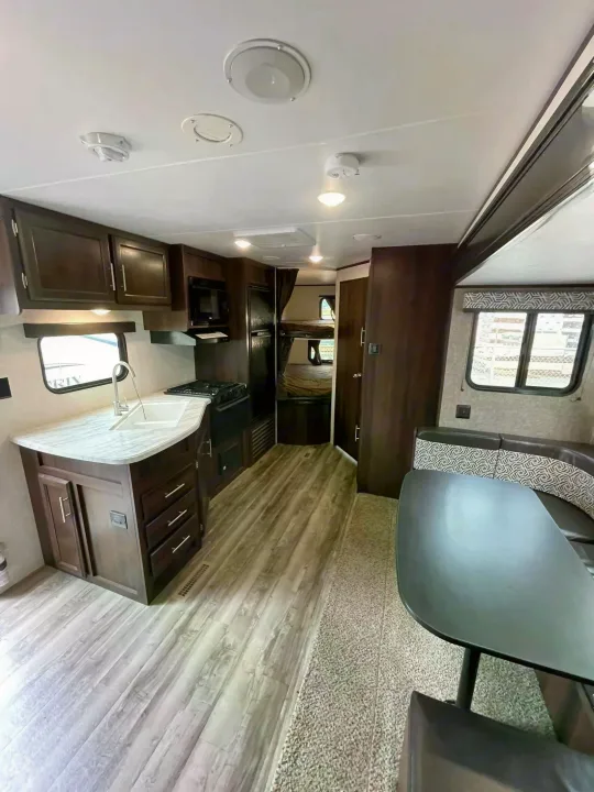 Spacious RV rental features a full kitchen with sink, stove, microwave, and fridge, plus a cozy dining booth and bunk beds.. Jayco Rocky Mountain 242BHSW 2019