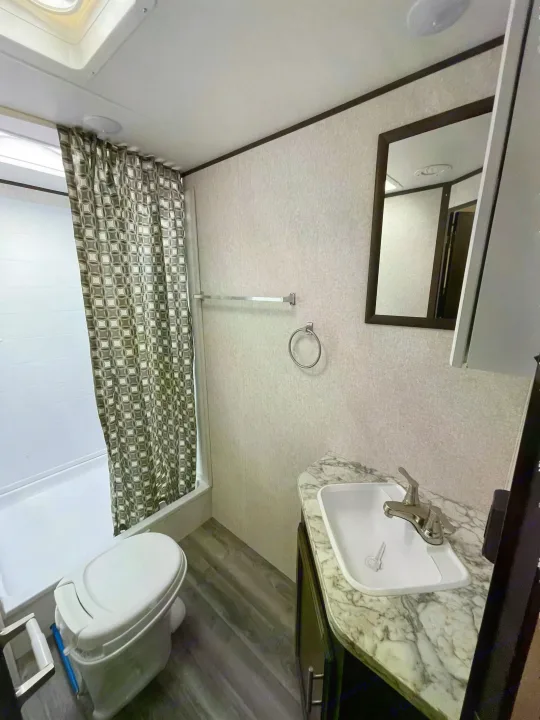 This clean RV rental bathroom features a compact toilet, shower with a grey patterned curtain, and a modern sink.. Jayco Rocky Mountain 242BHSW 2019