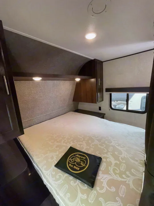 Comfortable RV rental bedroom interior with bed, overhead storage, and window, perfect for your next travel adventure.. Jayco Rocky Mountain 242BHSW 2019